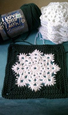 two crocheted squares are sitting on a bed with balls of yarn next to them