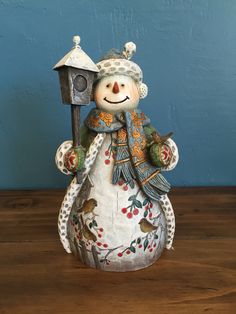 a snowman figurine holding a birdhouse on top of a wooden table