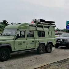 an army green vehicle parked next to a black car on the side of the road