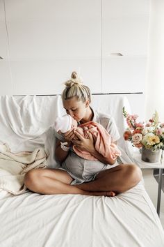 a woman holding a baby on top of a bed next to a vase with flowers