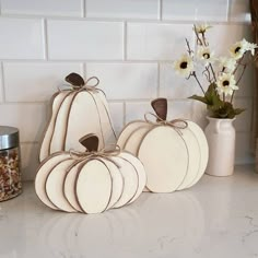 three white pumpkins sitting on top of a counter next to a vase with flowers