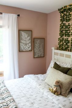 a bedroom with pink walls, white bedding and two framed pictures on the wall