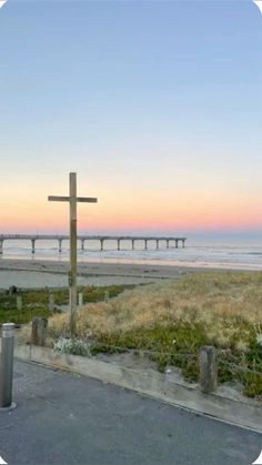 a wooden cross sitting on the side of a road next to the ocean at sunset