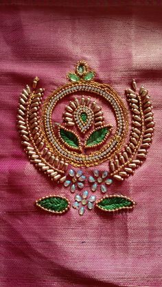 an embroidered piece on pink fabric with green leaves and flowers in the center, surrounded by jewels