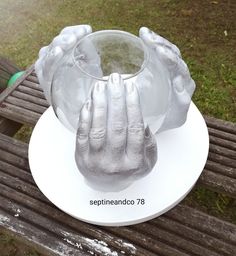 there is a silver sculpture on top of a white plate that has two hands in it