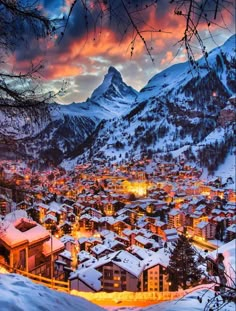 a snowy town with mountains in the background at sunset or dawn, surrounded by trees and snow covered hills