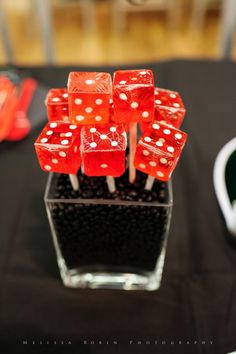 red and white dice on sticks in a clear glass vase with black table cloth behind it