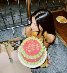 a woman holding a cake with candles on it in front of a gated area