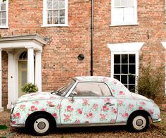 an old car parked in front of a brick building with flowers on it's side