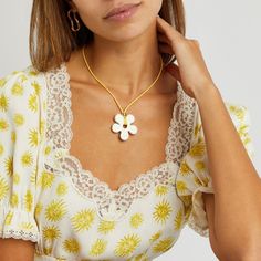 a woman wearing a yellow and white dress with a flower necklace on her neck, looking at the camera