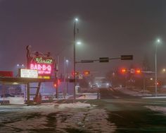 an empty street at night with snow on the ground and traffic lights in the background