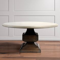 an oval marble table with wooden base in front of a white wall and wood floor