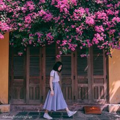 a woman walking down the street in front of pink flowers