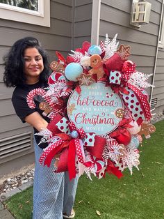 a woman standing in front of a house holding a christmas wreath that says, don't drink hot cocoa and santa is here