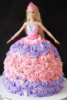 a barbie doll sitting on top of a pink and purple cake