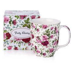 a white coffee cup with pink roses on it next to a boxed box for tea