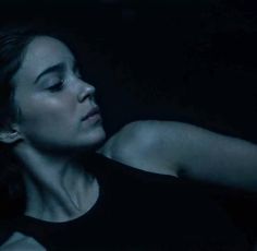 a woman laying down in the dark with her arm resting on her shoulder and eyes closed