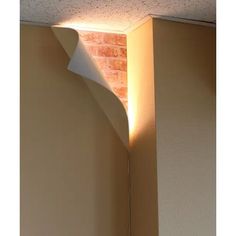 the corner of a room with a light coming from it's ceiling and a brick wall