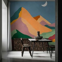 a dining table with two chairs in front of a colorful mountain mural on the wall