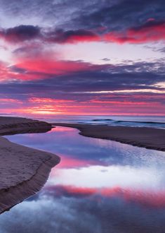 the sky is reflected in the water on the beach at sunset, with pink and purple clouds