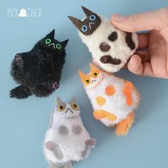 three small stuffed animals are being held up by someone's hand and another cat is sitting next to them