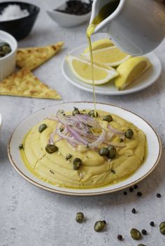 someone is pouring olives on top of a hummus