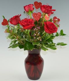 a vase filled with red roses and greenery