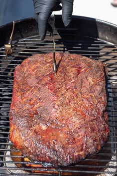 a steak being grilled on the grill with a pair of gloves over it's hands