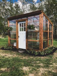 a small wooden structure with a white door and window in the middle of grass field