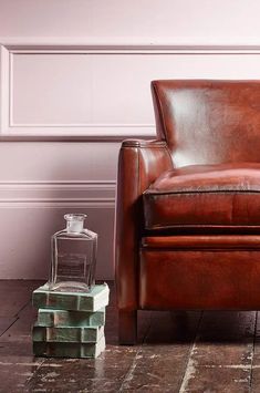 a brown leather chair sitting on top of a wooden floor next to a glass bottle