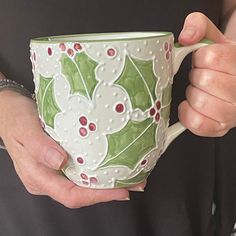 a person holding a green and white coffee cup with holly designs on it's side