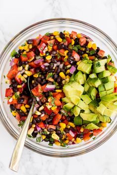 a glass bowl filled with black beans, avocado and corn salad next to a spoon