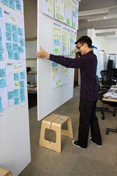 a man standing in front of a whiteboard with sticky notes on it and pointing to the wall