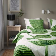 a green and white bed in a bedroom next to a lamp on a nightstand with a painting above it