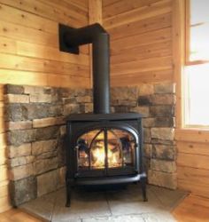 a wood burning stove sitting inside of a wooden room next to a window on top of a hard wood floor