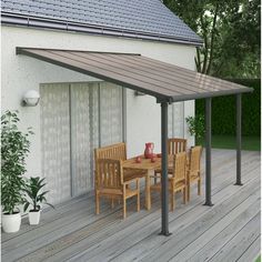 an outdoor dining table and chairs on a wooden deck next to a white wall with windows