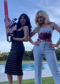 two women standing next to each other in front of a pool with a chainsaw