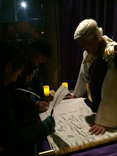 three people sitting at a table writing on paper