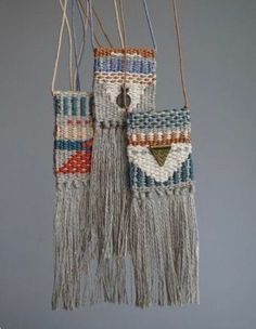 two bags are hanging from strings on the wall, one is made out of yarn and the other has tassels