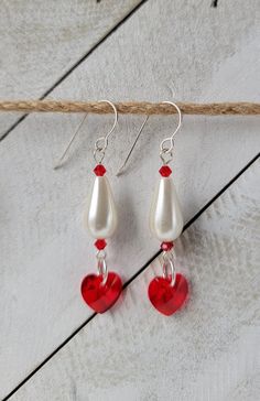 red and white heart shaped glass bead dangle earrings on a piece of wood