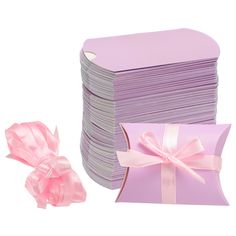 a stack of pink gift boxes next to a pile of white paper with ribbons on them