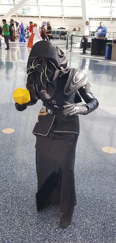 a person dressed up in black and holding a yellow object while walking through an airport