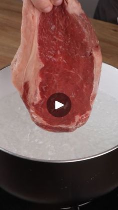 a raw piece of meat is being held up by someone's hand on top of a frying pan