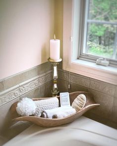 a candle and some knitted items in a wooden bowl on a bed with a window behind it