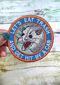 someone holding up a patch that says let's eat trash and get hit by a car