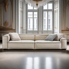 a white couch sitting in front of a window next to a chandelier on top of a wooden floor