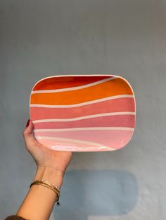 a hand holding an orange, pink and white striped serving platter in front of a gray wall