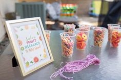 there are many cups with candy in them on the table next to a sign that says hello fruit necklace