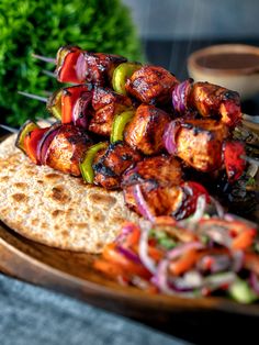 chicken kebabs with onions and peppers on a wooden platter next to a potted plant