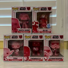 five star wars action figures are in their boxes on the counter, one is pink and the other is red